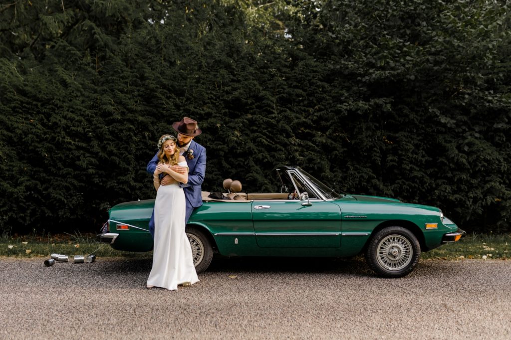 bride and groom leaning up against a classic car and hug each other