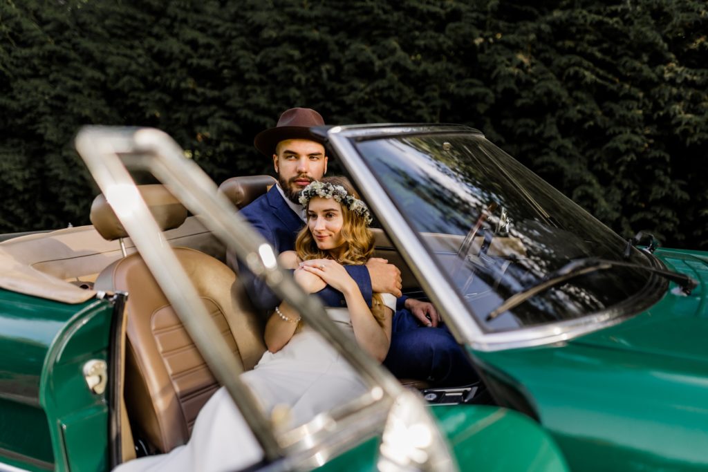 bride and groom in the classic car and smile into the distance