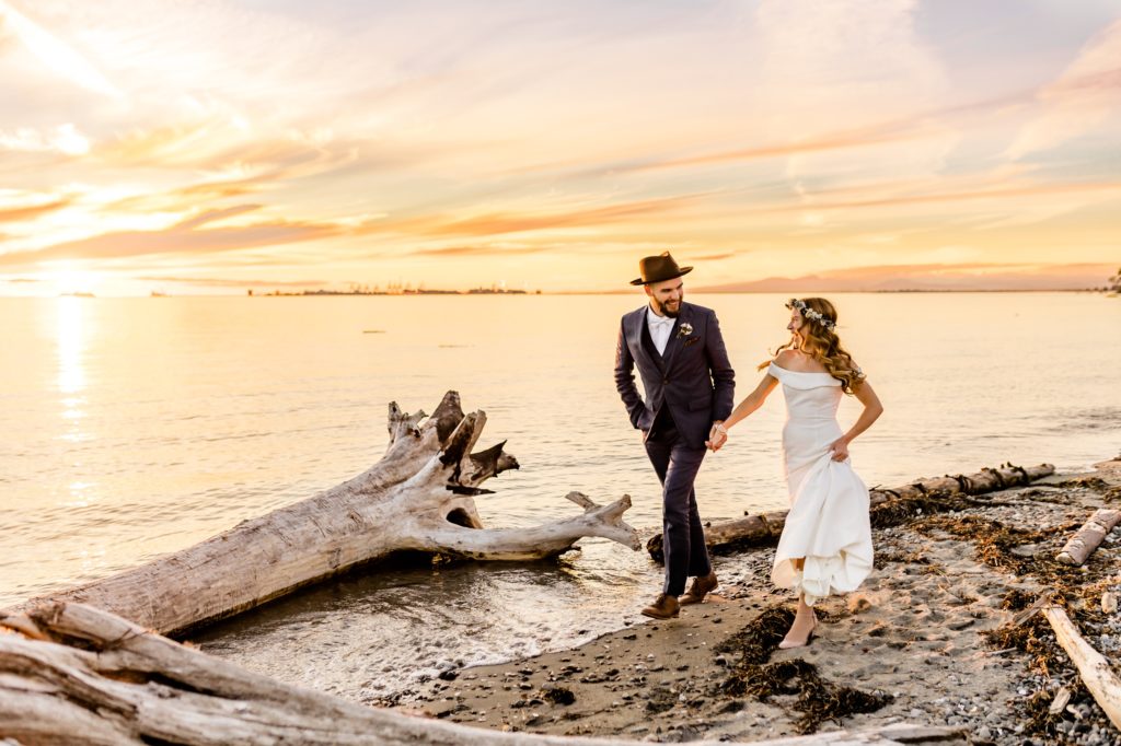 bride and groom run along the beach during sunset