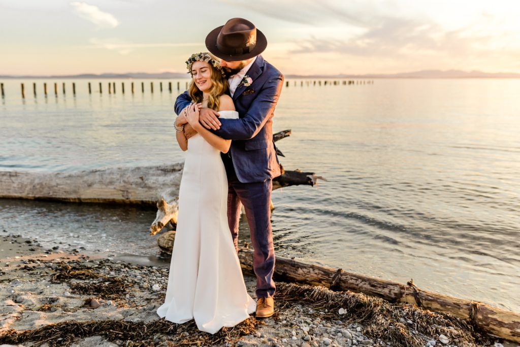 bride and groom snuggle the beach during sunset